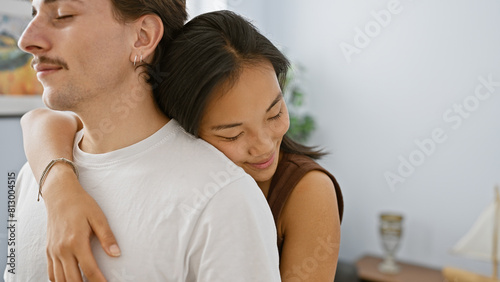 Intimate couple, asian woman, and hispanic man, embracing softly in a cozy apartment living room.