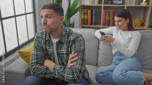 Upset man and woman using smartphone separately, highlighting relationship issues in a living room setting. photo