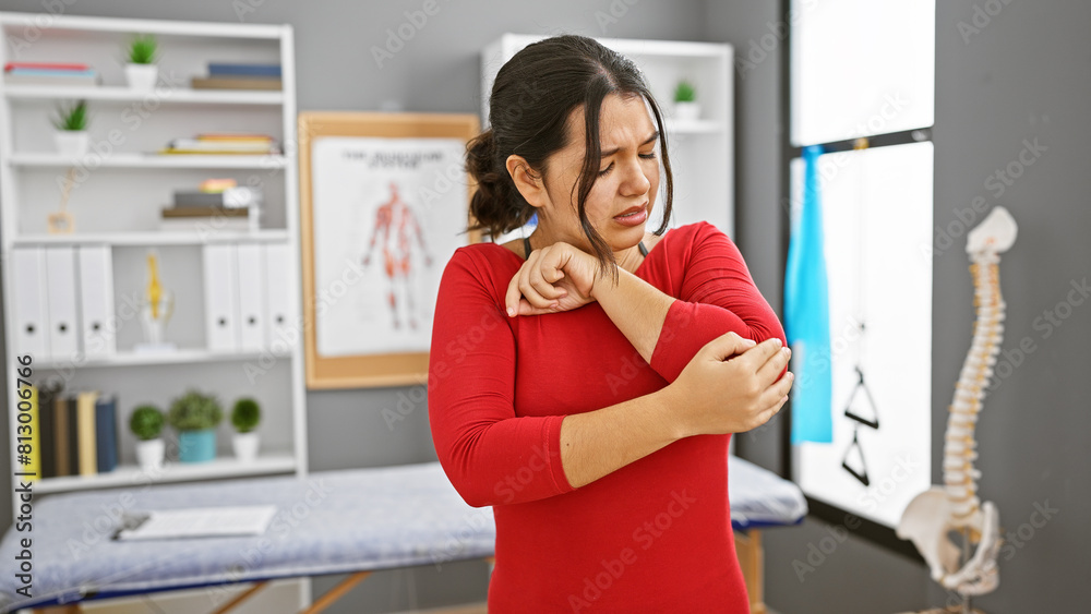 Hispanic woman in pain holding elbow at physical therapy clinic, showing discomfort and injury. Hispanic woman in pain holding elbow at physical therapy clinic, showing discomfort and injury.