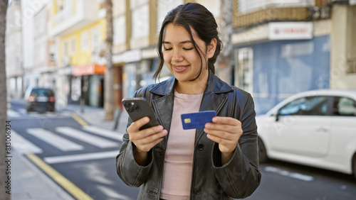 Young hispanic woman using a smartphone and holding a credit card on a city street. photo