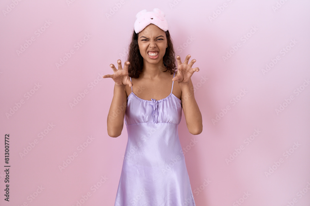 Young hispanic woman wearing sleep mask and nightgown smiling funny doing claw gesture as cat, aggressive and sexy expression Young hispanic woman wearing sleep mask and nightgown smiling funny doing claw gesture as cat, aggressive and sexy expression