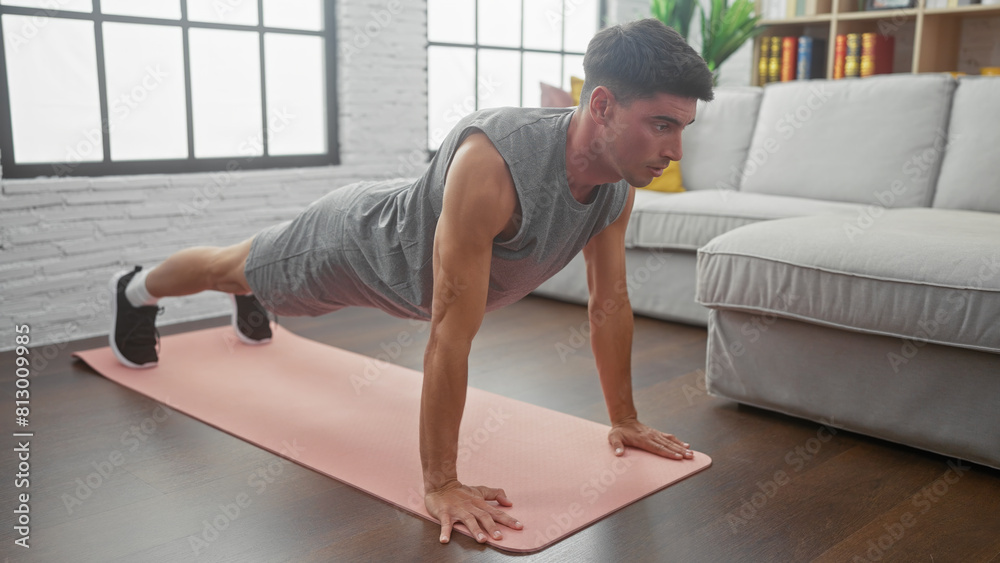 A young hispanic man does push-ups on a pink mat in a modern living room, showcasing fitness at home.