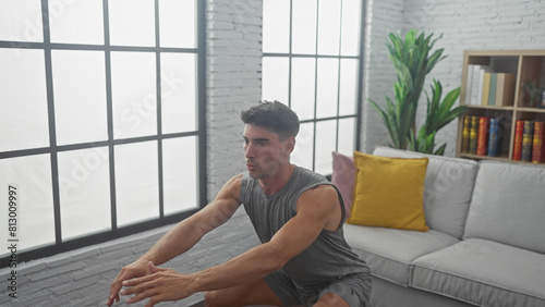 Handsome hispanic man stretching indoors on living room floor, displaying fitness and wellbeing in home interior.
