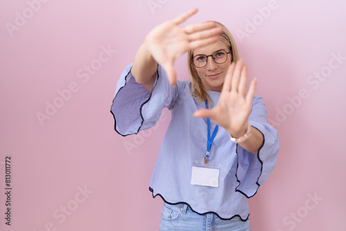 Young caucasian business woman wearing id card doing frame using hands palms and fingers, camera perspective photo