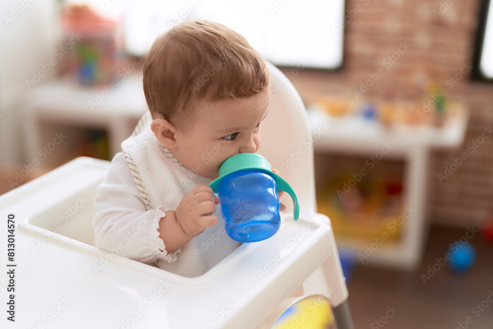 Adorable toddler sitting on baby highchair drinking water at kindergarten