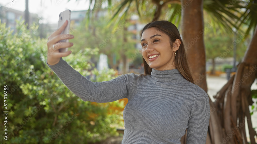 A young hispanic woman takes a selfie outdoors in a green park with tropical vegetation. A young hispanic woman takes a selfie outdoors in a green park with tropical vegetation.