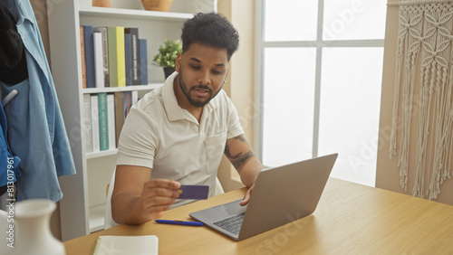 African american man using credit card for online shopping at home on laptop in a well-organized living room.