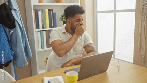 An adult african american man looks tired while working from home in a well-organized living room.