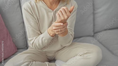 A young woman in casual wear sits indoors on a sofa  holding her wrist as if in pain or discomfort.