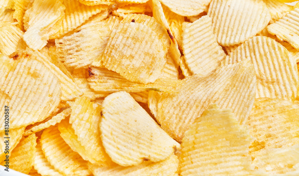 Close-up of golden crispy potato chips with ridges, filling the frame. Close-up of golden crispy potato chips with ridges, filling the frame.