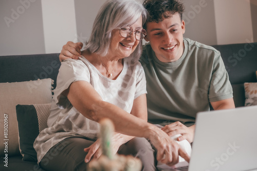 Happy young nephew teaching technology to his old grandmother using laptop. Senior woman learns to use computer, shopping online, make reservations