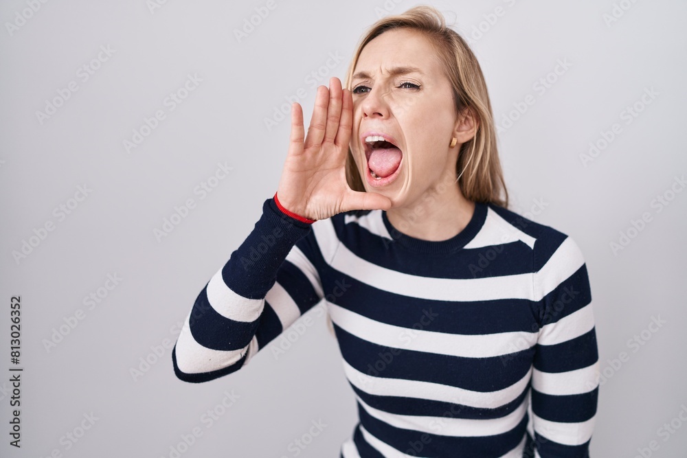 Young caucasian woman wearing casual navy sweater shouting and screaming loud to side with hand on mouth. communication concept. Young caucasian woman wearing casual navy sweater shouting and screaming loud to side with hand on mouth. communication concept.