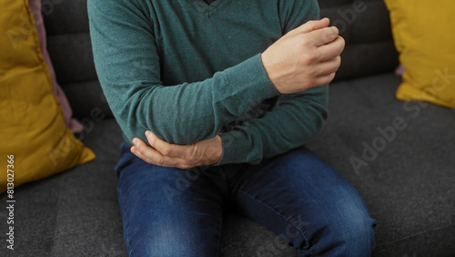 Young caucasian man holding elbow in pain at home, portraying an indoor discomfort scenario.