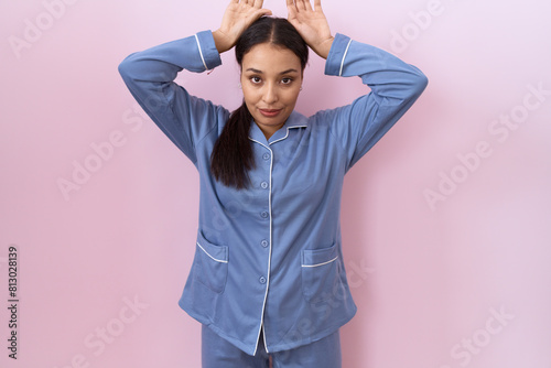 Young arab woman wearing blue pajama doing bunny ears gesture with hands palms looking cynical and skeptical. easter rabbit concept. photo