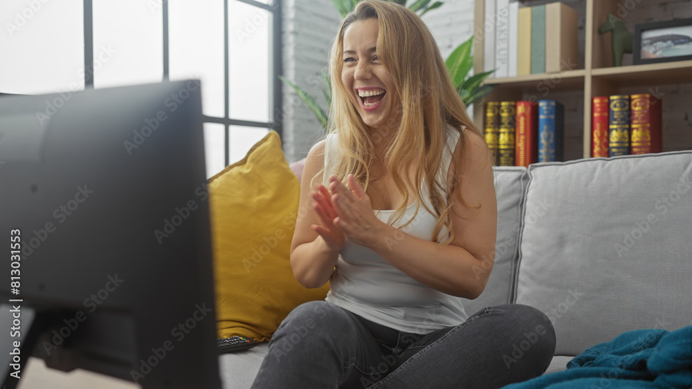 A joyful caucasian woman applauding indoors while watching tv in her cozy living room, showcasing a modern home atmosphere