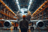 A skilled worker stands in awe as he gazes at the massive airplane before him in an industrial hangar, appreciating the intricate engineering