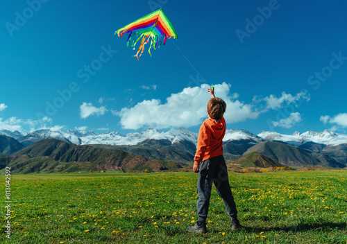 Happy boy with kite on green field on mountains background