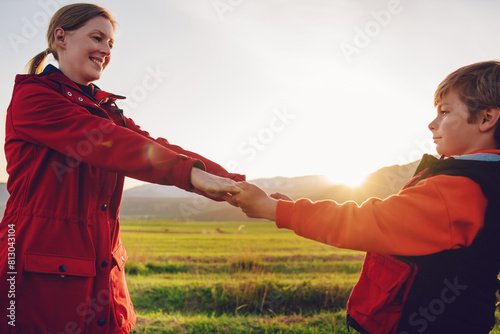 Happy mother and son tourists look at each other and holding hands in a picturesque mountain valley at sunset