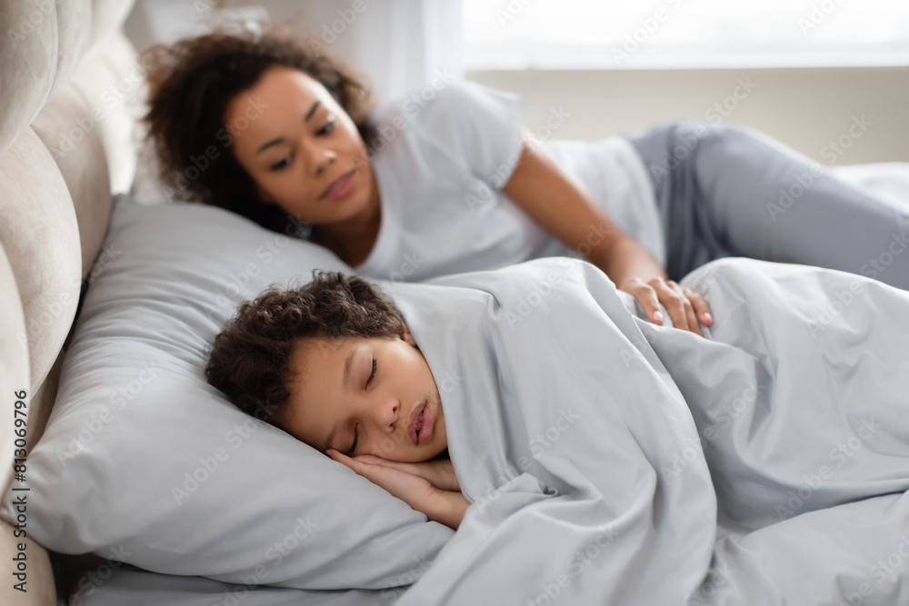 African American woman and child peacefully sleeping side by side on a comfortable bed with white sheets. The mother and child are both lying on their sides African American woman and child peacefully sleeping side by side on a comfortable bed with white sheets. The mother and child are both lying on their sides