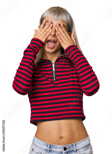Young caucasian young woman in studio covers eyes with hands, smiles broadly waiting for a surprise.
