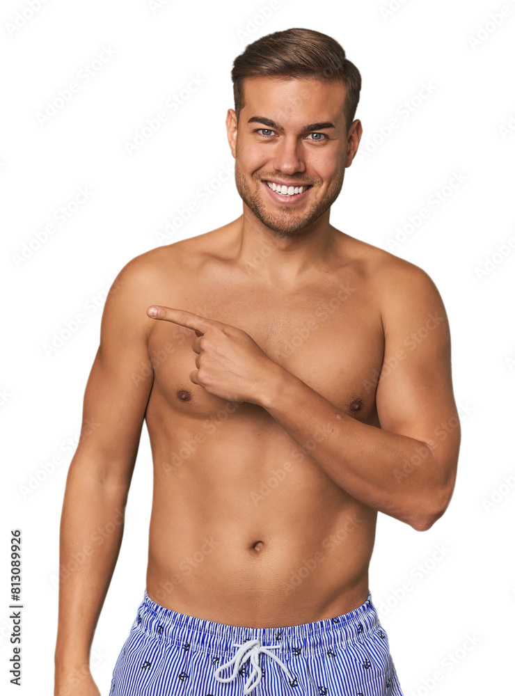 Young man shirtless in swimwear, studio smiling and pointing aside, showing something at blank space. Young man shirtless in swimwear, studio smiling and pointing aside, showing something at blank space.