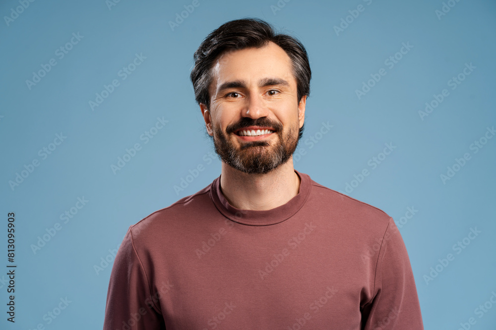 Smiling bearded man wearing casual posing in studio isolated on blue, looking at camera Smiling bearded man wearing casual posing in studio isolated on blue, looking at camera
