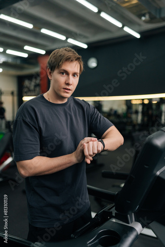 Vertical portrait of handsome sportsman check health indicator and heart rate on smartwatch during workout strength training  looking at camera. Athlete using fitness tracker during workout.