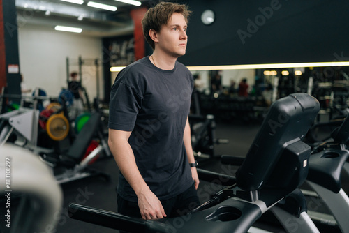 Portrait of male beginner wearing outfit walking on treadmill, working on health and fitness in gym. Athletic young man warming-up run routine exercise at sport club. Concept of healthy lifestyle