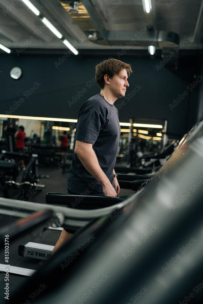 Vertical shot of beginner sportsman having intensive cardio workout to burn calories in gym. Side view of young athletic man jogging on gym machine, having cardio session in well-equipped fitness club Vertical shot of beginner sportsman having intensive cardio workout to burn calories in gym. Side view of young athletic man jogging on gym machine, having cardio session in well-equipped fitness club