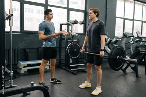 Obraz na plátně Wide shot of beginner sportsman doing barbell press during weightlifting workout with help of personal trainer at sport club