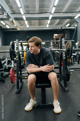 Vertical portrait of beginner sportsman having accident injury and hurt at arms while workout and weight training at gym. Athletic man suffering from muscle injury while exercising at sport club.