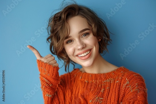 A woman, wearing an orange sweater, cheerfully gives a thumbs up gesture.