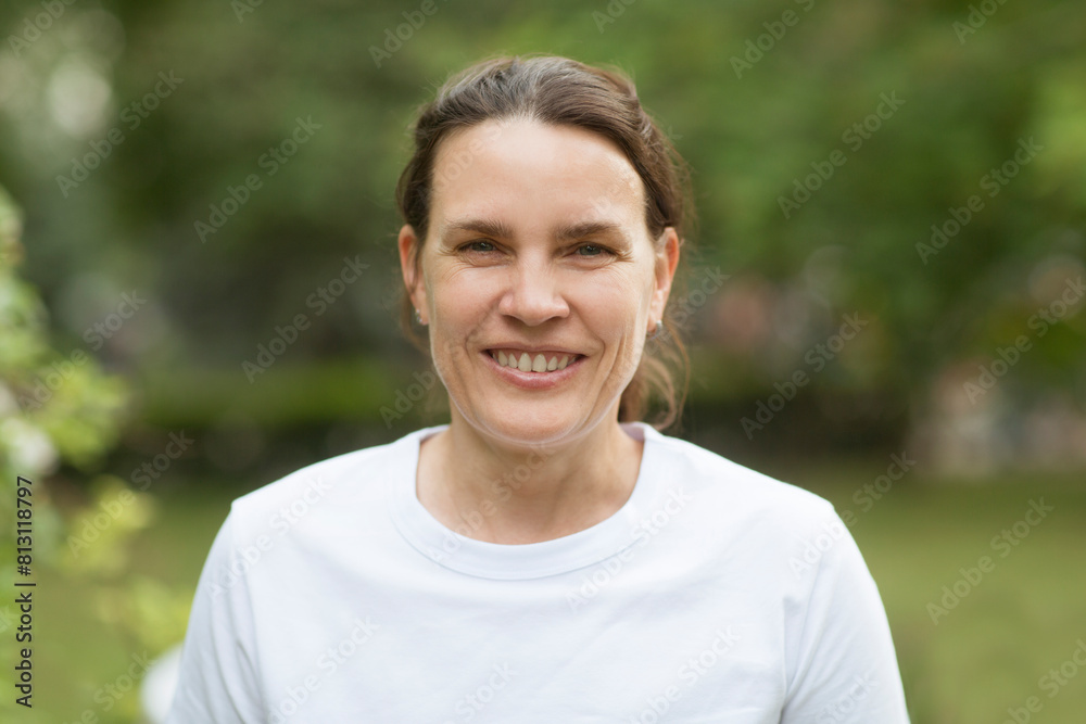 middle aged woman in a white T-shirt relax smiles and looks at the camera against the backdrop of nature. burnout syndrome middle aged woman in a white T-shirt relax smiles and looks at the camera against the backdrop of nature. burnout syndrome