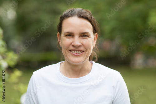 middle aged woman in a white T-shirt relax smiles and looks at the camera against the backdrop of nature. burnout syndrome