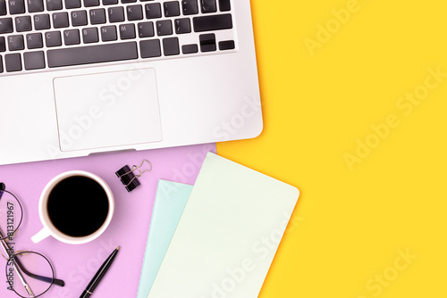 Workspace with laptop, cup of coffee and stationery on a purple and yellow background. Online education concept with place for text.