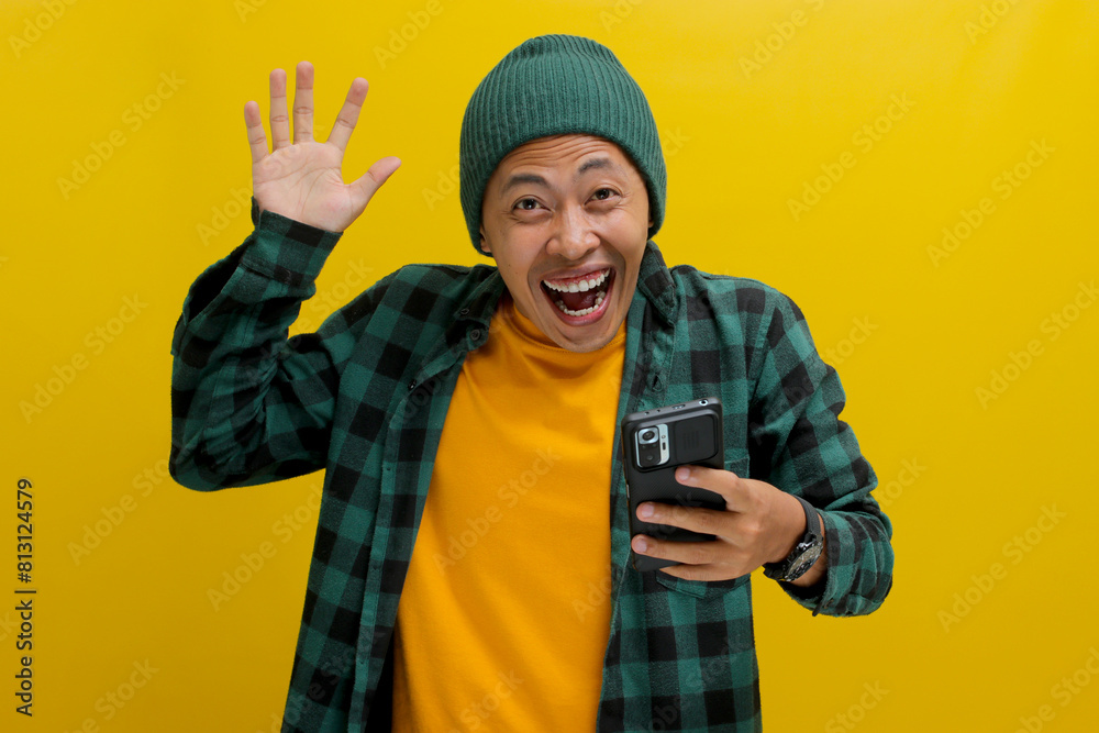 Happy Asian man wearing a beanie hat and casual shirt smiles broadly, displaying excitement and surprise while looking at his phone. Thrilled, reading messages on a dating app or receiving good news Happy Asian man wearing a beanie hat and casual shirt smiles broadly, displaying excitement and surprise while looking at his phone. Thrilled, reading messages on a dating app or receiving good news