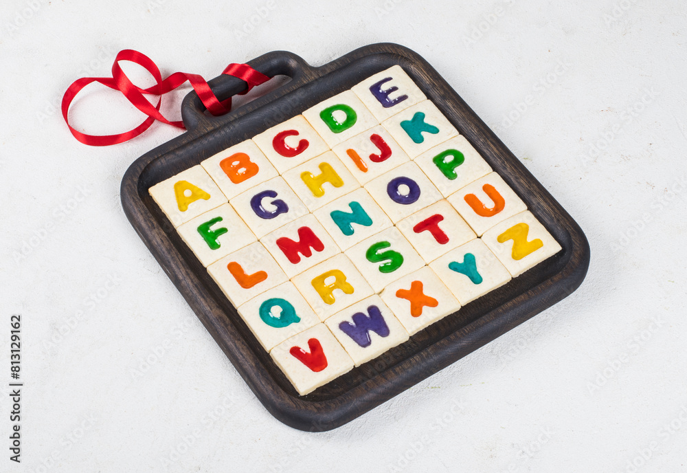 Cookies English Alphabet. Square cookies with colored marmalade filling in the shape of English letters. On a dark wooden plate with a red satin ribbon. Cookies English Alphabet. Square cookies with colored marmalade filling in the shape of English letters. On a dark wooden plate with a red satin ribbon.