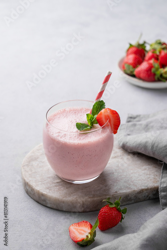 A glass of fresh strawberry smoothie with mint on a marble board on a light background with fresh berries and napkin.