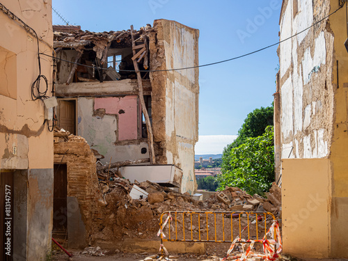 Vista de un edificio en ruinas con una valla amarilla de aviso, piedras  y restos de construcción con peligro de derrumbe. Verano de 2021 España.