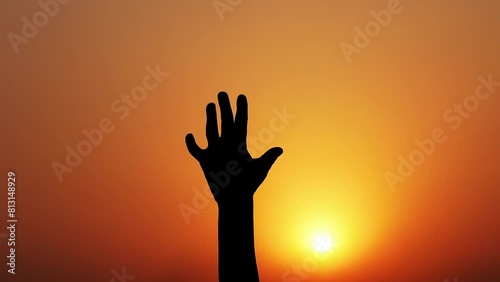 A child's hands clenching and unclenching against a background of yellow-orange light at sunset. photo