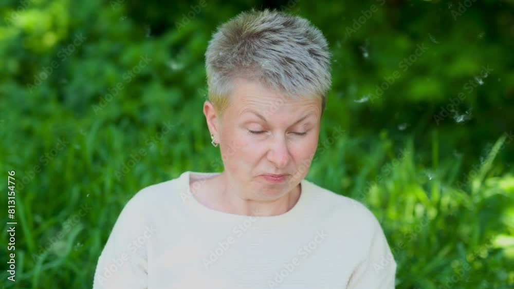 Caucasian woman sneezes and blows her nose into a paper napkin against a green background. Spring exacerbation of allergy to poplar fluff. Allergy in adults hay fever Caucasian woman sneezes and blows her nose into a paper napkin against a green background. Spring exacerbation of allergy to poplar fluff. Allergy in adults hay fever