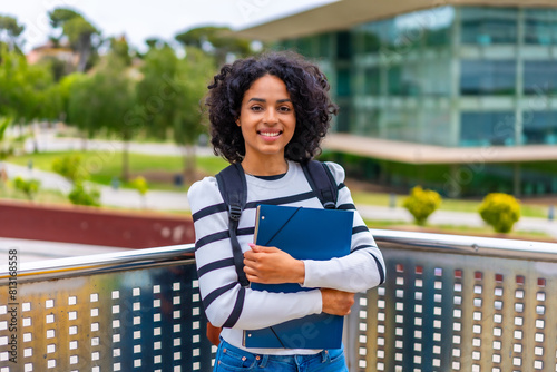 Smiling latin student standing proud with folder outside the university