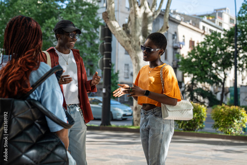 Joyful African American youths friends engaged in conversation while strolling city streets, exchanging laugh, smiles. Happy fun black young people students talk on street telling interesting stories.