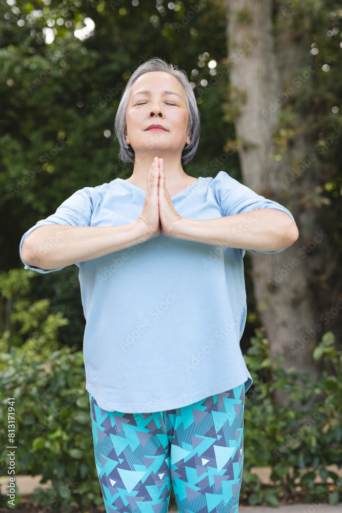 A senior Asian female practicing yoga outdoors with blue background A senior Asian female practicing yoga outdoors with blue background