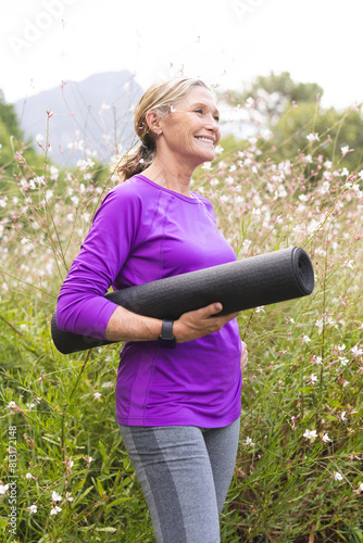 Enjoying outdoors, caucasian senior female holding a yoga mat stands in a field