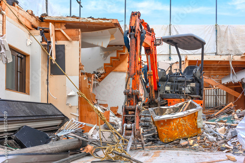 An orange backhoe loader equipped with a hydraulic excavator attachment to be able to grab heavy debris during the destruction of a traditional japanese wooden house.