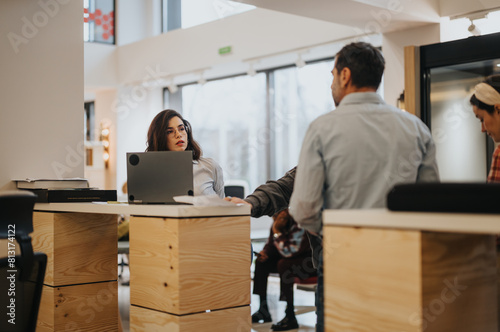 Focused businesswoman using laptop at workplace with team members conversing in the backdrop of a modern office setting.