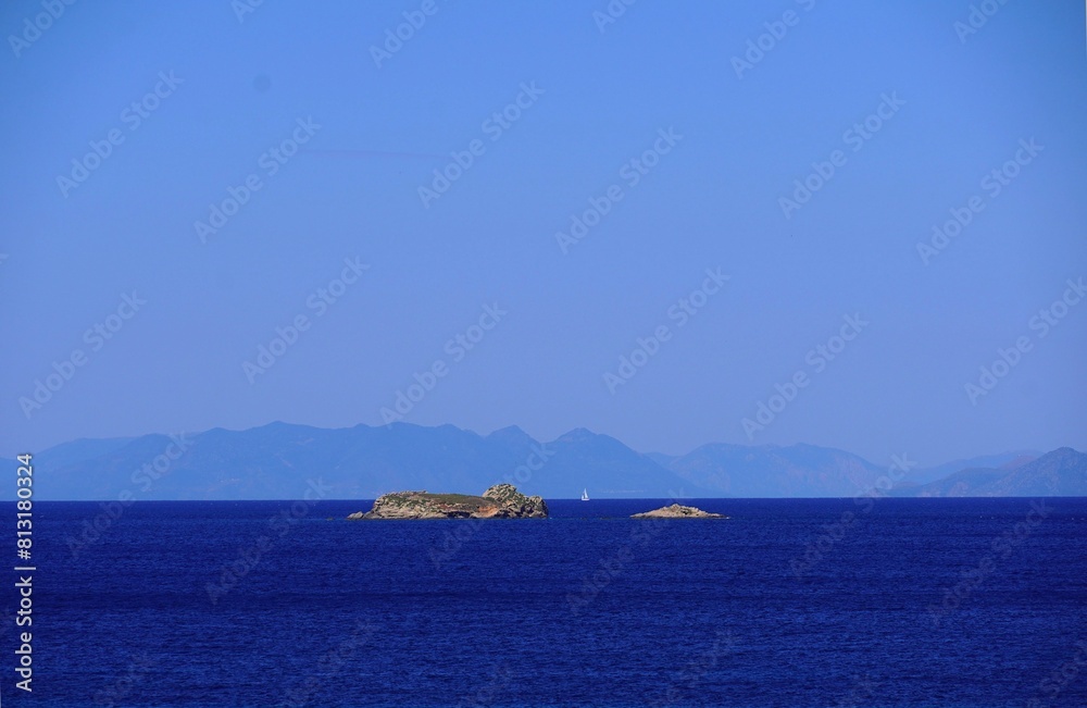 A white sailboat between two small islands, near the coast of Attica, Greece