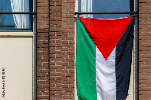 The flag of Palestine hanging outside the window of building, Tricolor of three equal horizontal stripes (black, white, and green with a red triangle) overlaid by a red triangle issuing from the hoist