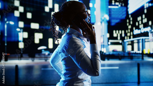 African american woman strolling around cityscape at night, enjoying conversation over the phone with husband. Businesswoman walking home from work having telephone call to make commute go faster photo